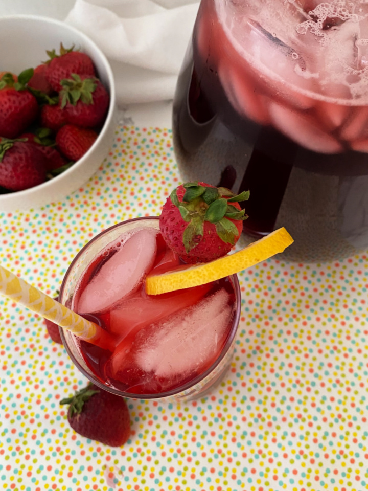pitcher of hibiscus iced tea with strawberries and a glassful of tea and ice